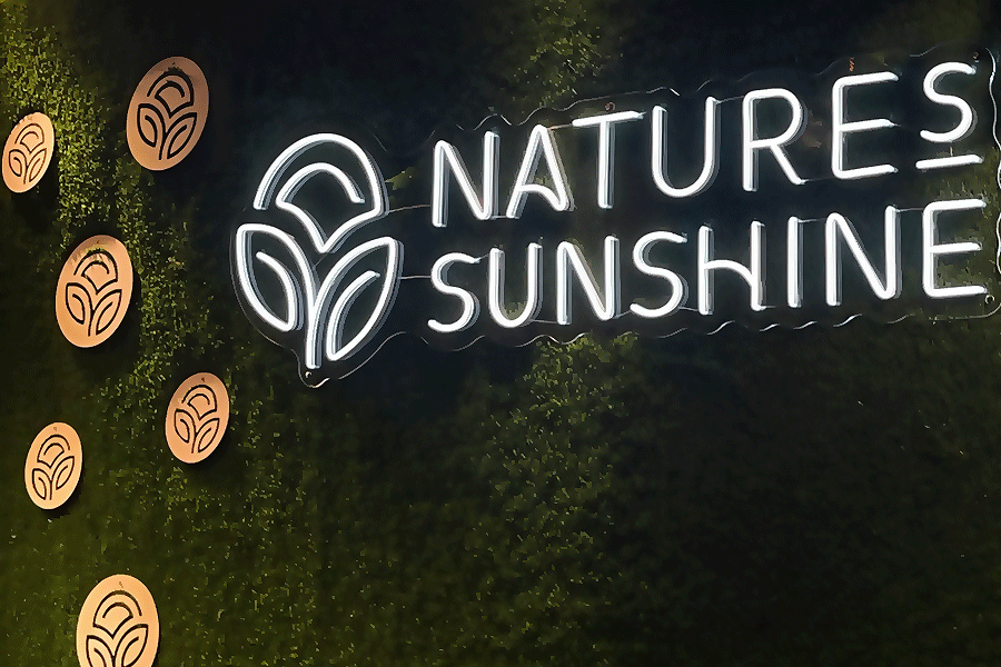 Valkoinen LED-neonlogo “Natures Sunshine” vihreällä sammalseinällä puisten logokiekkojen kanssa vastaanottotilassa