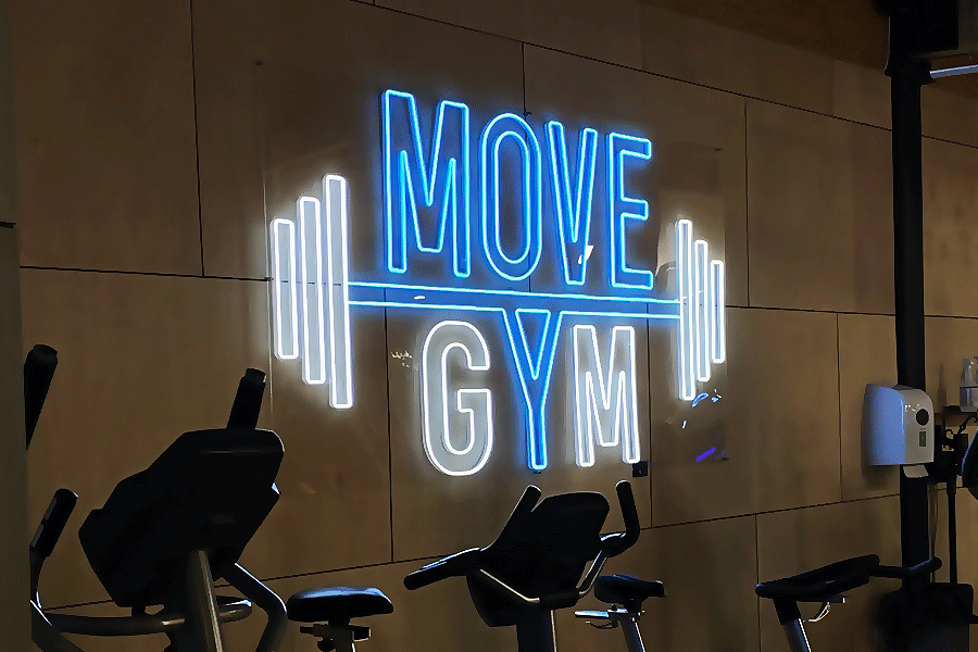 LED-neonskylt ”MOVE GYM” i blått och vitt ovanför motionscyklar på ett gym